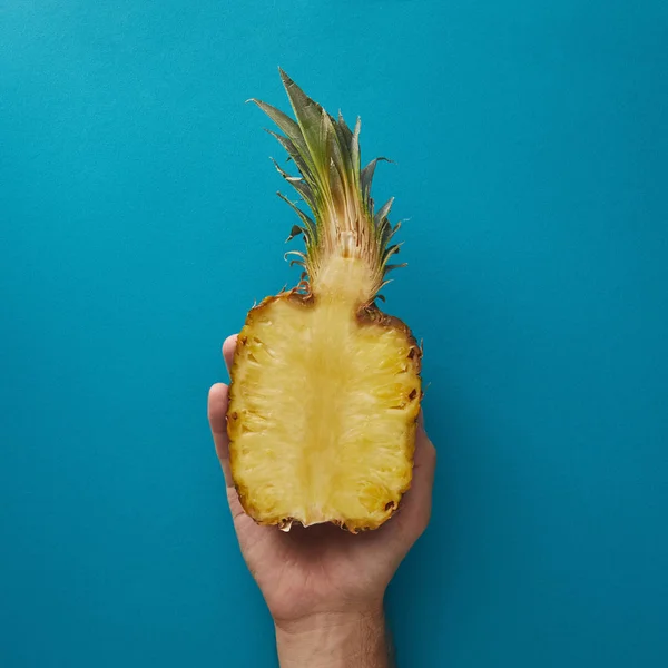 Cropped image of man holding half of ripe pineapple above blue surface — Stock Photo