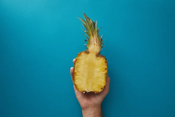 Cropped image of man holding half of ripe pineapple above blue surface — Stock Photo