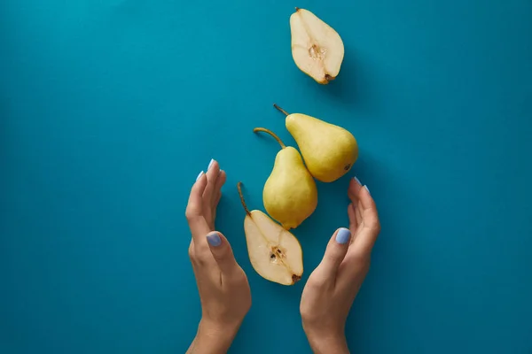 Cropped image of woman holding hands near pears above blue surface — Stock Photo