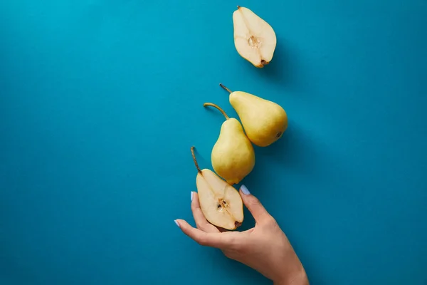 Cropped image of woman taking half of pear from blue surface — Stock Photo