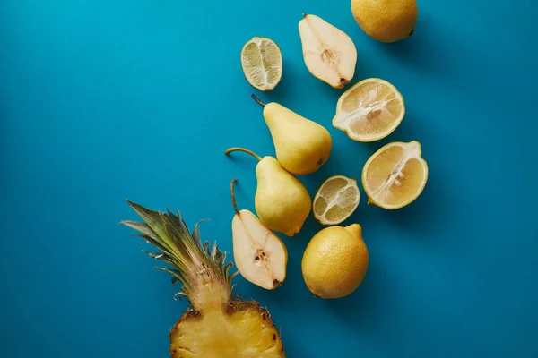 Вид сверху на ананас, груши и лимоны на голубой поверхности — стоковое фото