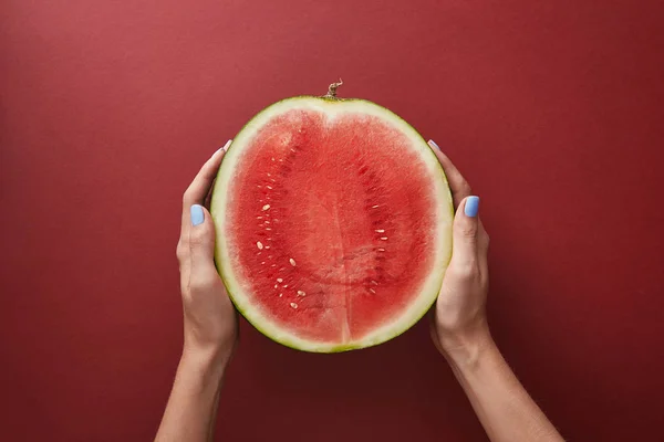 Abgeschnittenes Bild einer Frau, die die Hälfte der Wassermelone über der roten Oberfläche hält — Stockfoto