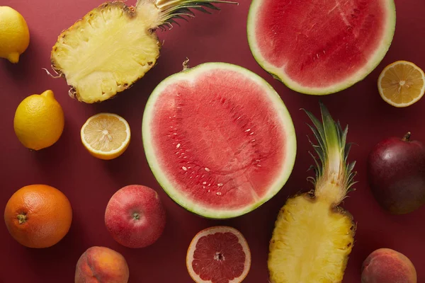 Elevated view of cut watermelon and pineapple on red surface — Stock Photo