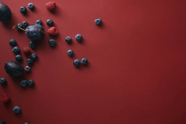 Top view of blueberries, raspberries and plums on red surface — Stock Photo