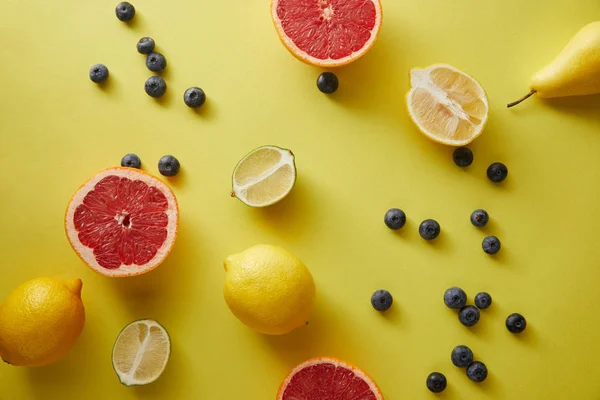 Вид сверху на грейпфруты, лимоны, лаймы и чернику на желтую поверхность — стоковое фото