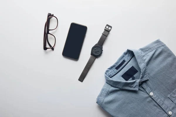 Vista superior de camisa, smartphone y gafas aisladas en blanco - foto de stock