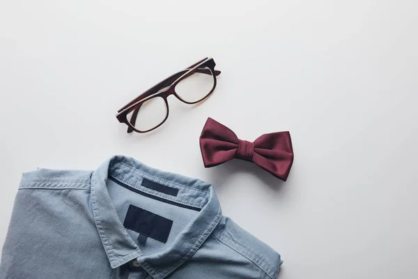 Vue de dessus de chemise bleue, noeud papillon bordeaux et lunettes isolées sur blanc — Photo de stock