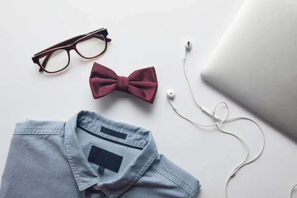 Top view of blue shirt, burgundy bow tie, glasses and laptop with earphones isolated on white — Stock Photo
