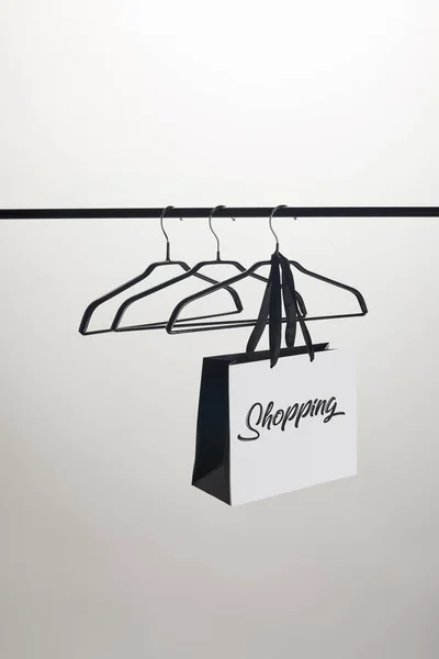 Paper bag with word shopping and empty hangers on stand isolated on white — Stock Photo