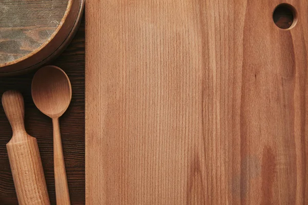 Vista superior de tabla de cortar de madera, cuchara, rodillo y tamiz en la mesa - foto de stock