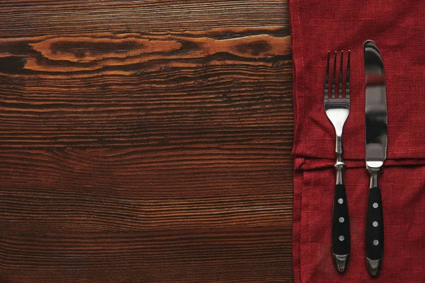 Вид сверху на вилку и нож на темно-красную скатерть на деревянном столе — стоковое фото