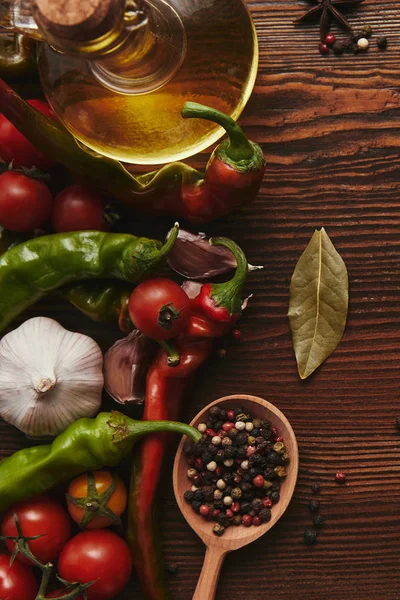 Vista superior de la cuchara de madera con granos de pimienta, aceite y verduras frescas en la mesa - foto de stock