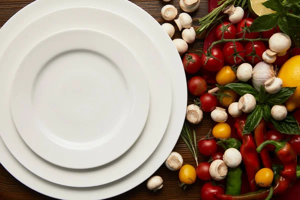 Top view of empty round white plates and fresh vegetables on wooden surface — Stock Photo