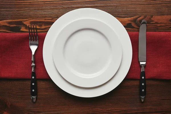 Top view of round empty white plates with fork and knife on wooden table — Stock Photo