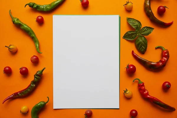 Vue du dessus de la carte blanche et tomates fraîches avec basilic et poivrons sur orange — Photo de stock
