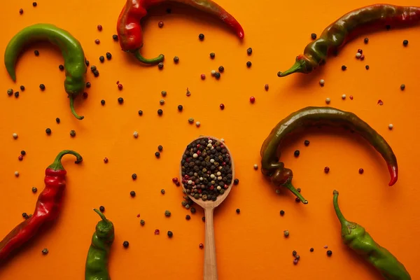 Top view of chili peppers and peppercorns in wooden spoon on orange — Stock Photo