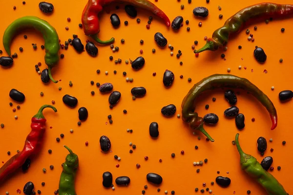 Top view of chili peppers, haricot beans and peppercorns on orange background — Stock Photo