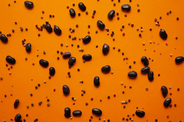 Vue du dessus des haricots et des grains de poivre sur fond orange — Photo de stock