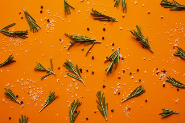 Vue du dessus du romarin, du sel et des grains de poivre sur fond orange — Photo de stock