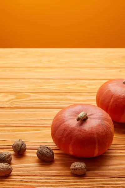 Vista de cerca de calabazas naranjas maduras y nueces en la superficie de madera - foto de stock