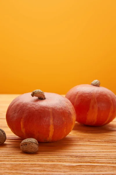 Крупный план спелых тыкв и грецких орехов на деревянной поверхности на оранжевом фоне — стоковое фото