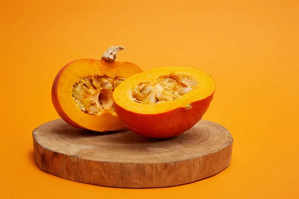 Close-up view of ripe sliced pumpkin on round wooden board on orange background — Stock Photo