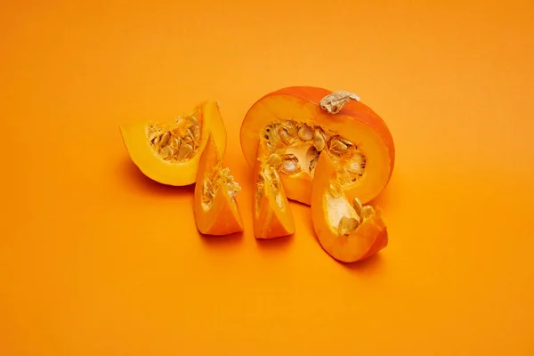 Close-up view of ripe sliced pumpkin with seeds on orange background — Stock Photo