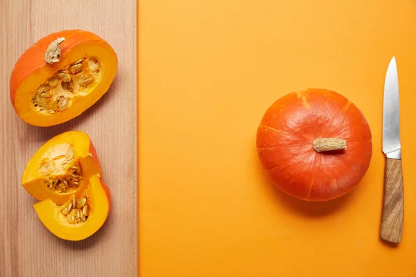 Vista superior de abóboras inteiras e fatiadas e faca na superfície laranja e de madeira — Fotografia de Stock