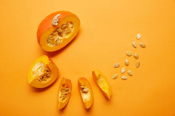 Верхний вид спелых нарезанных тыкв с семенами на оранжевом фоне — стоковое фото