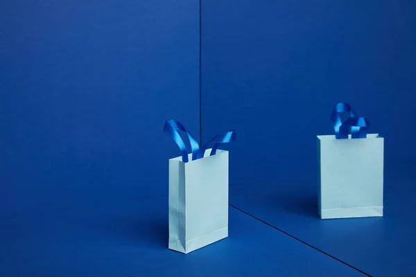 Vista de cerca de la bolsa de compras de papel con reflejo de espejo sobre fondo azul - foto de stock