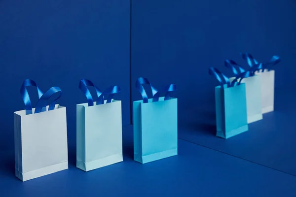 Close up view of arranged paper shopping bags with mirror reflection on blue background — Stock Photo