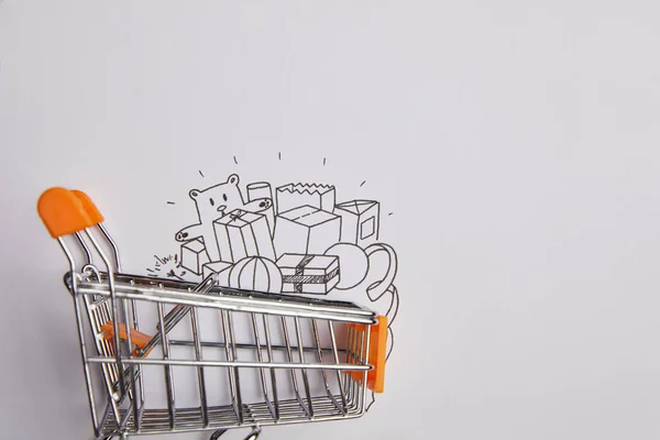 Top view of shopping cart with little goods made of paper on grey background — Stock Photo