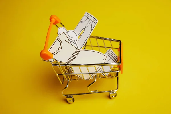 Close up view of little shopping trolley with paper clothes on yellow backdrop — Stock Photo