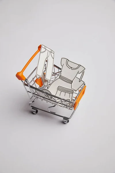 Vista de perto do carrinho de compras com pouca roupa feita de papel sobre fundo cinza — Fotografia de Stock