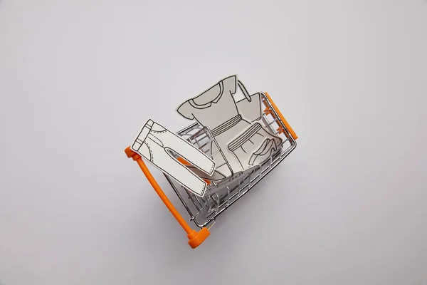 Top view of shopping cart with little clothes made of paper on grey background — Stock Photo