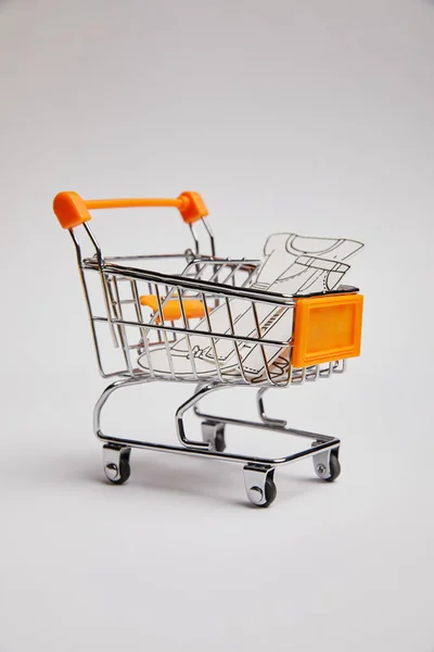 Close up view of shopping cart with little clothes made of paper on grey background — Stock Photo