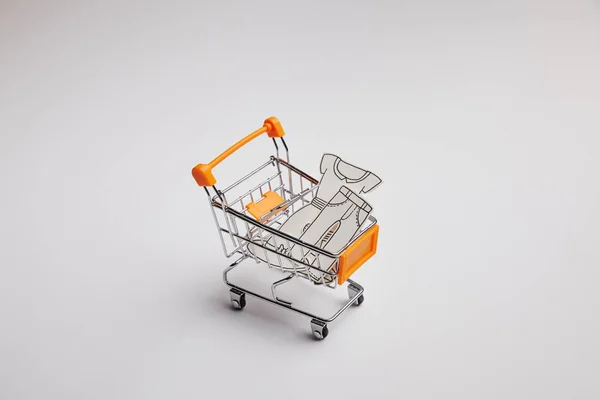 Close up view of shopping cart with little clothes made of paper on grey background — Stock Photo