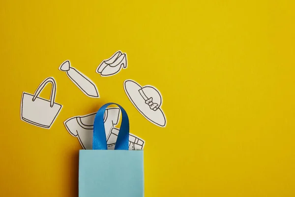 Vue du dessus du sac à provisions bleu avec des vêtements en papier sur fond jaune — Photo de stock