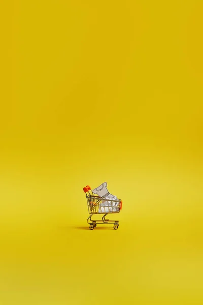 Close up view of little shopping trolley with paper clothes on yellow backdrop — Stock Photo