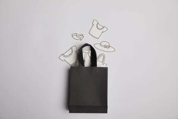 Vue du dessus du sac à provisions noir et des vêtements en papier sur fond gris, concept de magasinage — Photo de stock