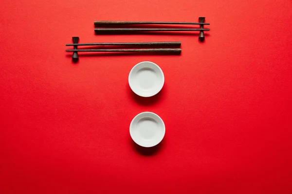 Flat lay with arranged empty bowls and chopsticks on red background — Stock Photo