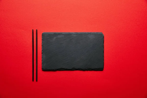 Top view of empty black slate plate for sushi and chopsticks isolated on red — Stock Photo