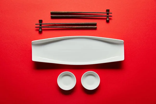 Flat lay with arranged empty bowls, plate and chopsticks on red background — Stock Photo