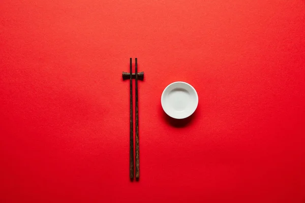 Vue de dessus des baguettes disposées et bol vide sur fond rouge — Photo de stock