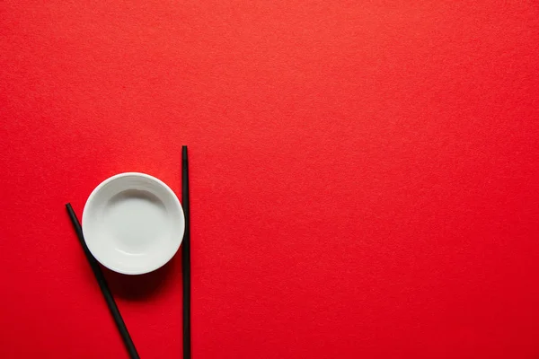 Top view of arranged chopsticks and empty bowl on red backdrop — Stock Photo