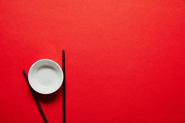 Vue de dessus des baguettes disposées et bol vide sur fond rouge — Photo de stock