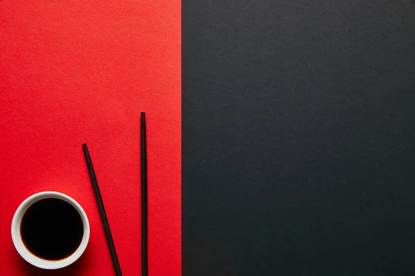 Вид зверху соєвого соусу в мисці та паличках на червоно-чорному тлі — стокове фото