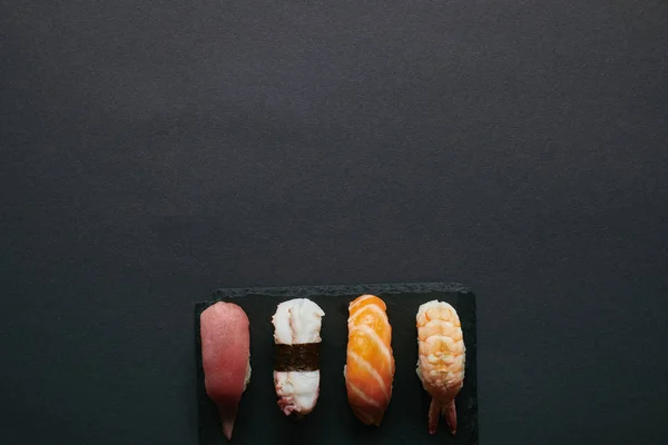 Вид сверху на разнообразные суши из нигири, установленные на черной доске на черном столе — стоковое фото