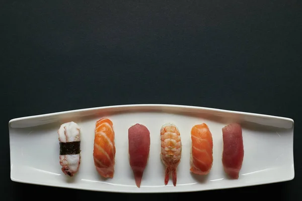Vue du dessus des sushis nigiri assortis sur plaque blanche à la surface sombre — Photo de stock