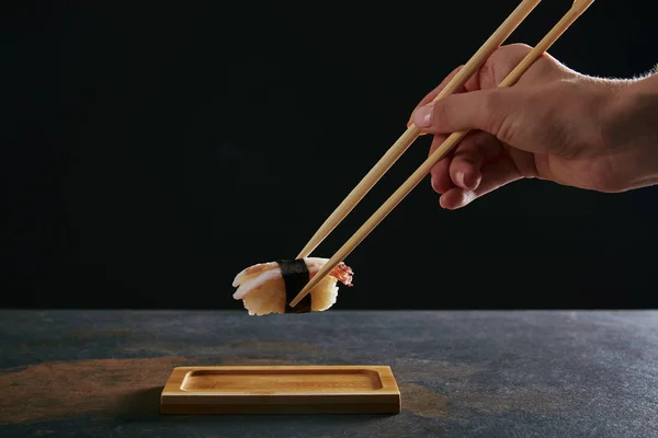 Vista parcial de la mujer sosteniendo nigiri sushi con camarones sobre fondo negro - foto de stock